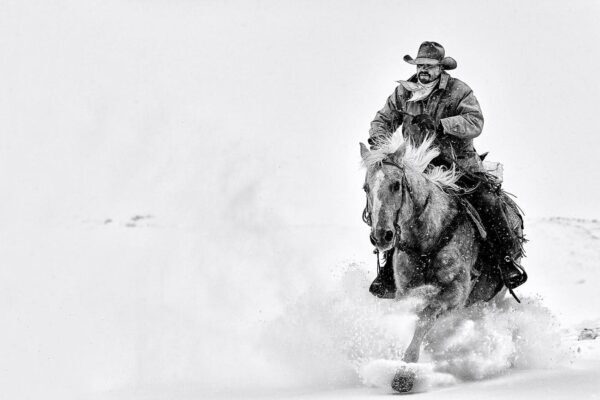 cowboy riding horse alone in snow black and white fine art photography